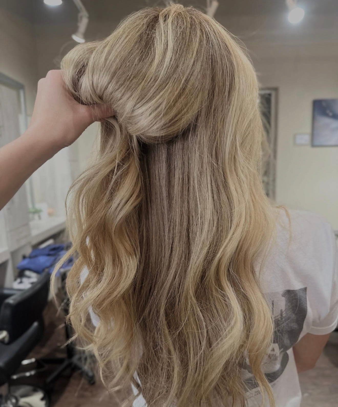 A stylist lifting the top section of long blonde hair to check the blend underneath at Lee Graves Salon