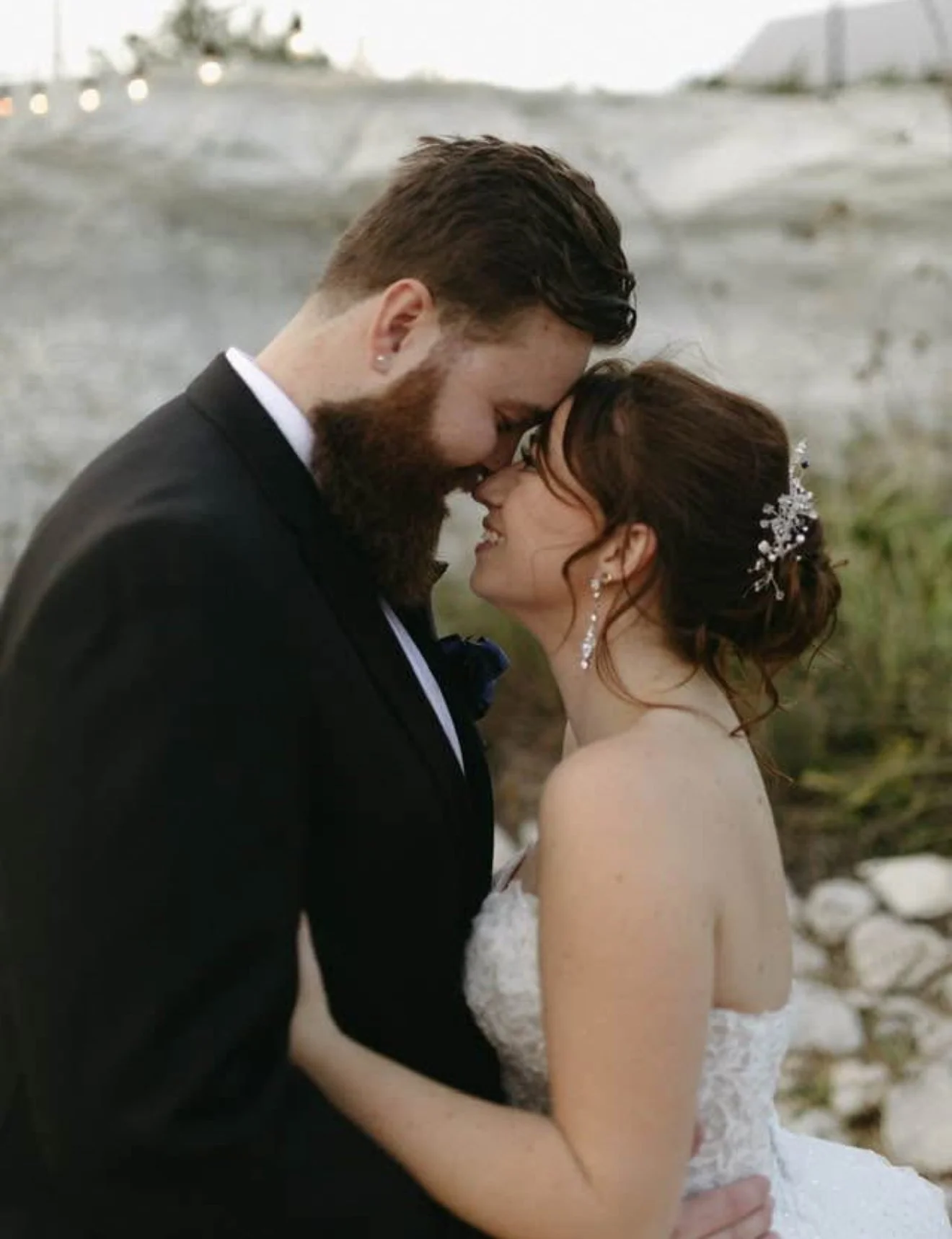 A groom with a full, shaped beard and short sides beside his bride on their wedding day