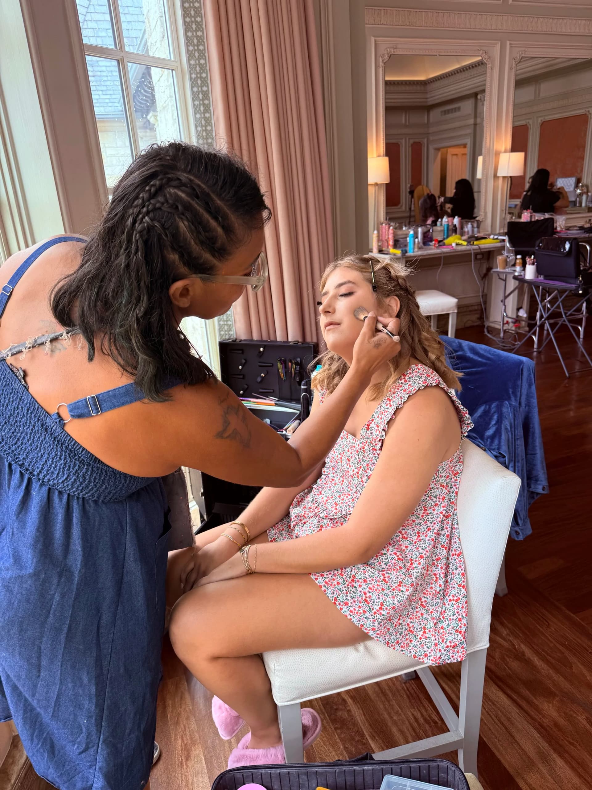 A makeup artist working on a member of the bridal party in a venue getting-ready suite