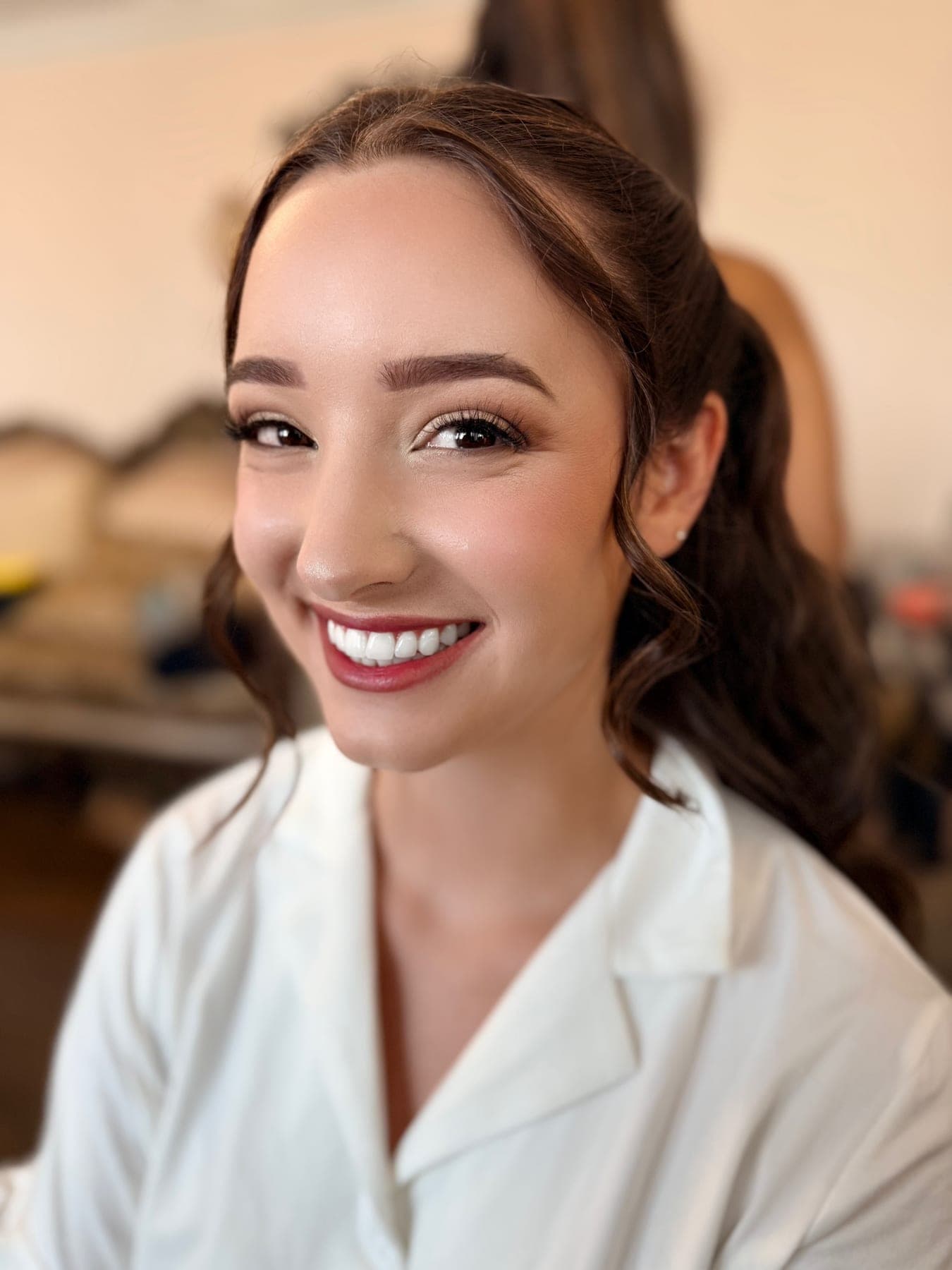A bride smiling in a white robe with her finished soft glam wedding makeup