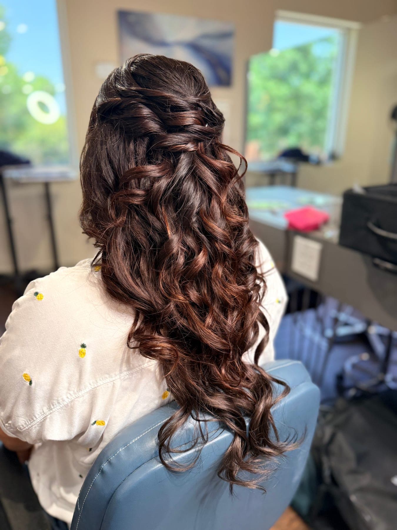 Braided half-up style pinned at the crown over long brunette curls